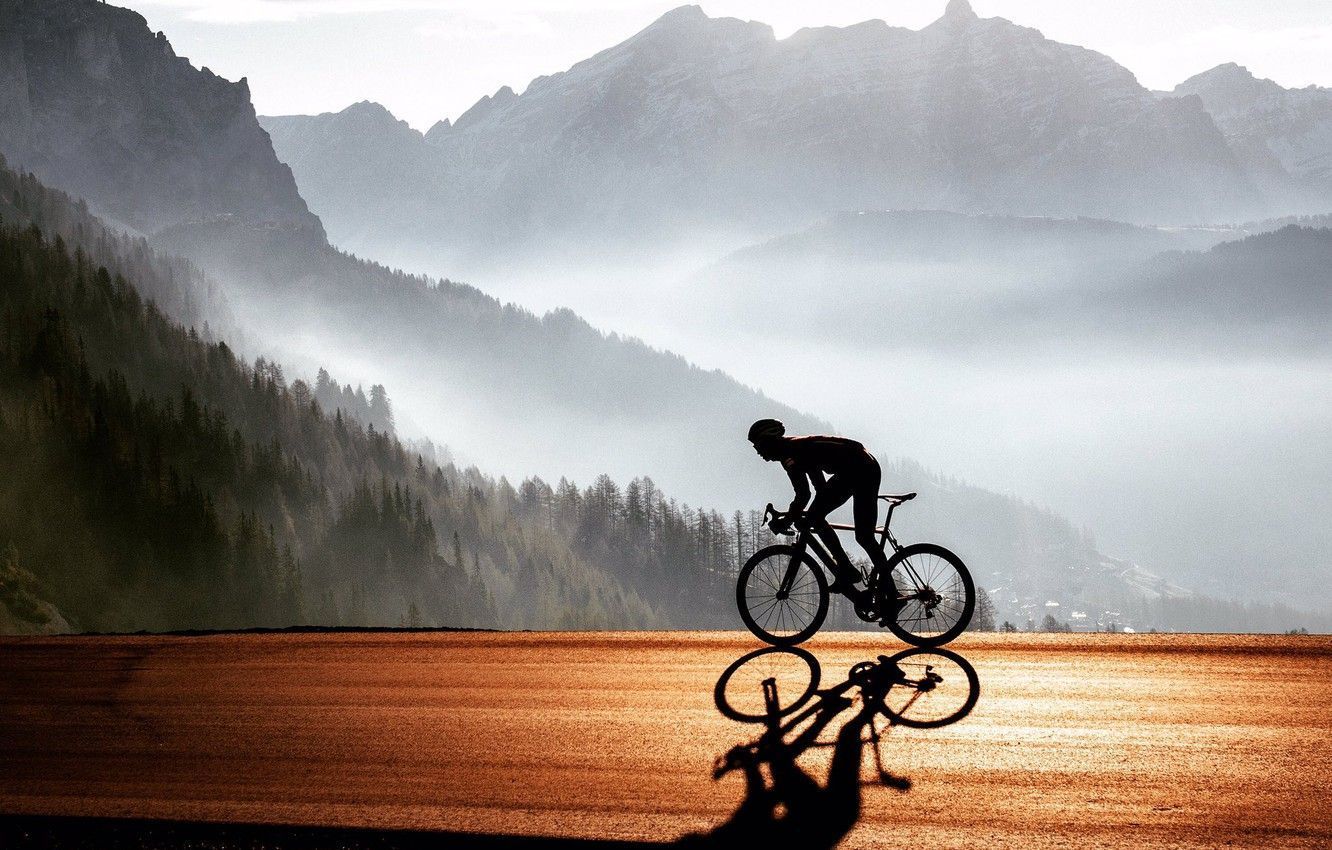 A silhouette of a cyclist against a misty mountain background